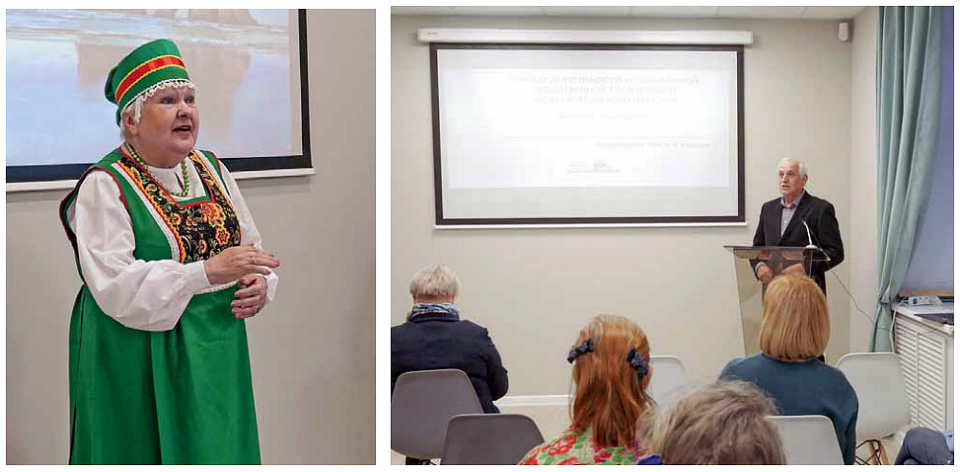 Varttunut nainne vihreässä karjalaisessa kansallisasussa esittää laulun ja varttunut mies tummassa puvussa pitää esitystä yhdistyksen toiminnasta valkokankaan edessä