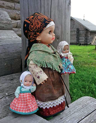 Kolme nukkea harmaan mökin portailla