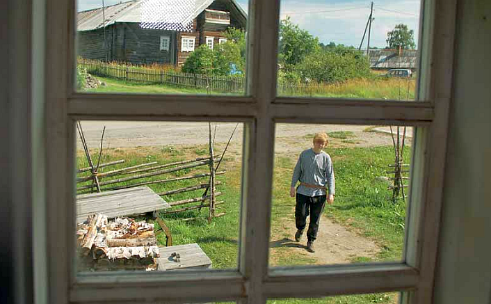 Näkymä ikkunasta ulos ja pihalla kävelee nainen polulla kesällä