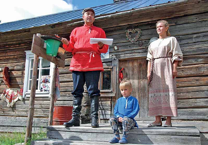 Perhe talon portailla. Mies, nainen ja ja poika karjalaisissa puvuissa.