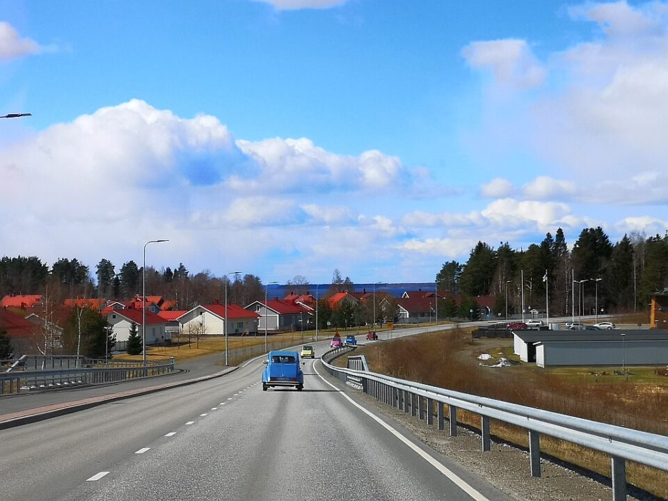 Harmaata asfalttitietä jolla on sininen auto ja taivas on kirkkaan sininen.