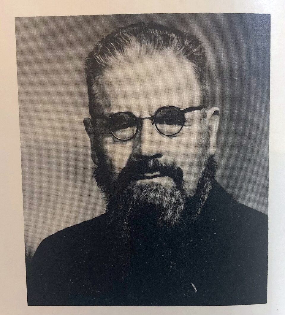 Mustavalkoinen kuva parrakkaasta miehestä silmälaseissa mustassa paidassa