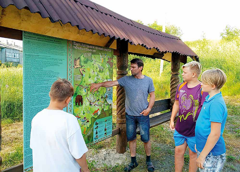 Mies osoittaa karttataulua kun kolme poikaa vieressä katsovat häntä
