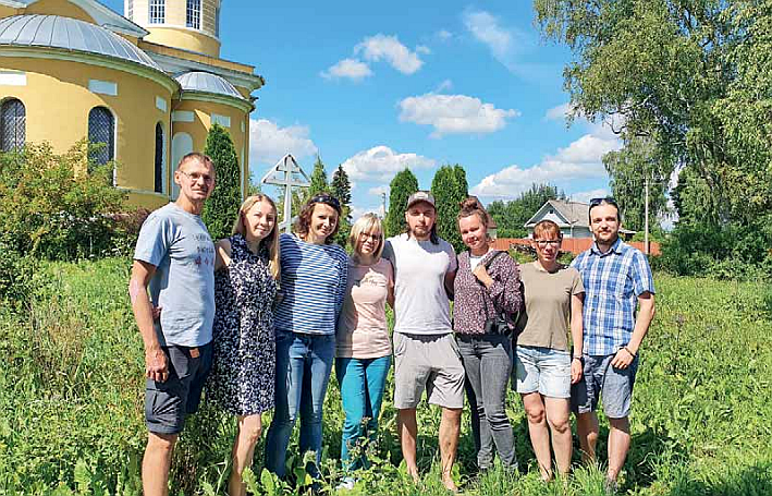 Ryhmä miehiä ja naisia seisomassa nurmikolla keltaisen rakennuksen edessä