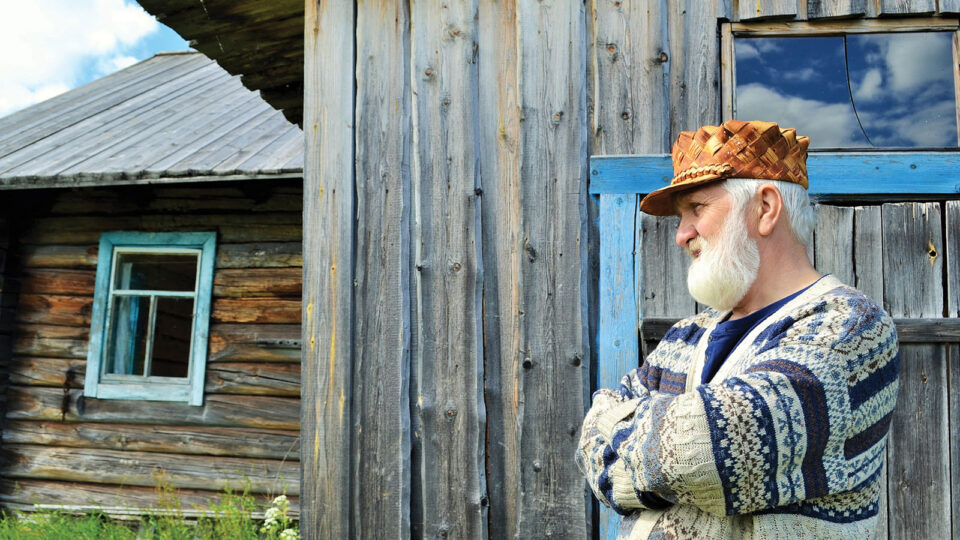 Mies seisoo kädet puuskassa talon kulmallla ja katsoo jonnekin kauas.
