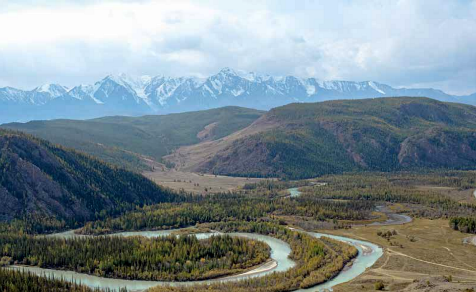 Näkymä vuoristoon, jonka edessä on metsää ja joki