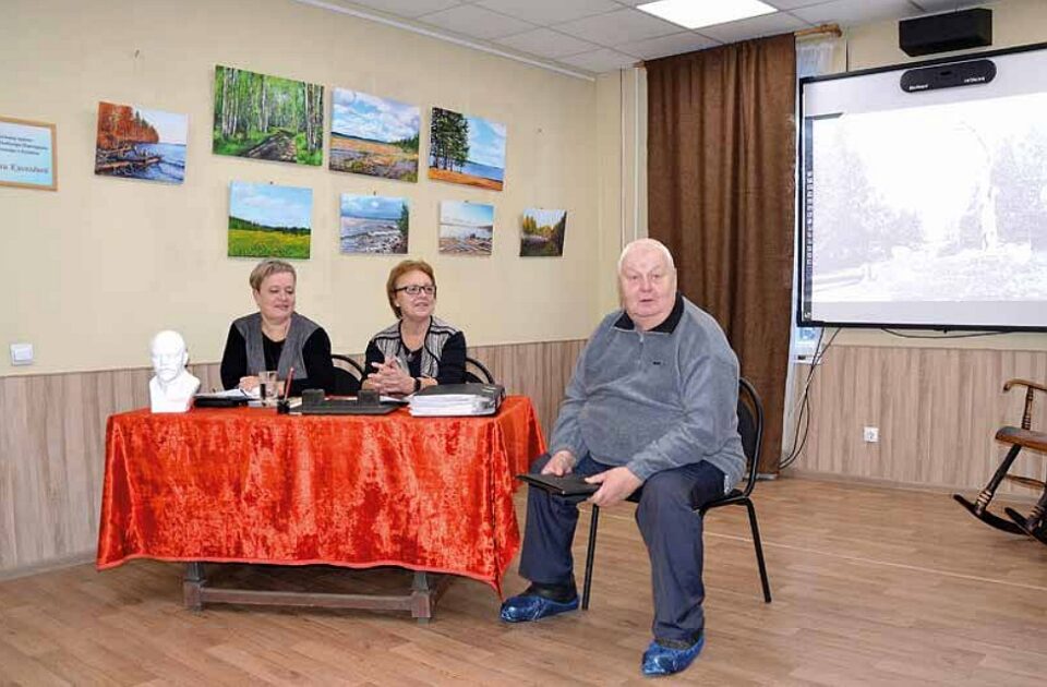Kaksi naista istuvat pöydän takana ja yksi mies istuu pöydän vieressä