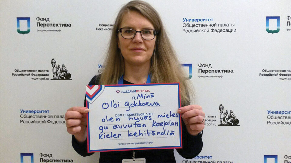 Nainen pitää kädessään paperikylttiä, jota hän näyttää kameralle.