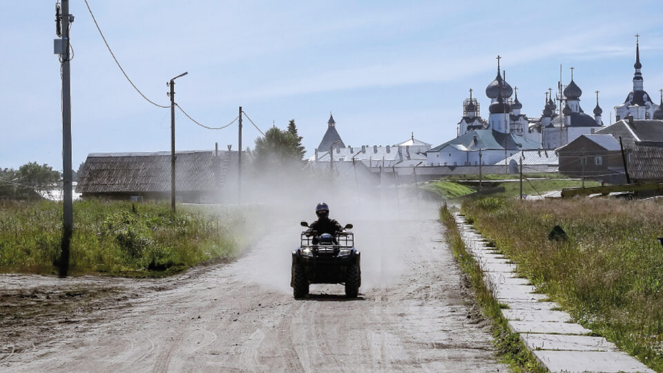 Kypäräpäinen henkilö ajaa mönkijällä kohti kameraa hiekkatiellä, joka pöllyää.