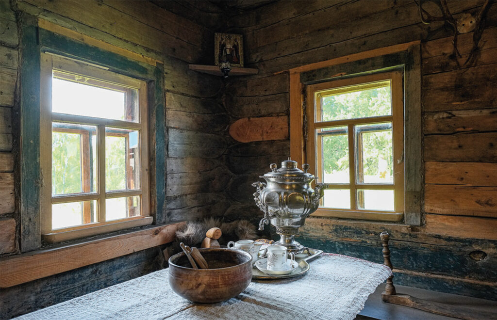 Pöydällä ikkunoiden äärellä on samovaari, teekuppeja tarjotttimella ja suuri kulho.