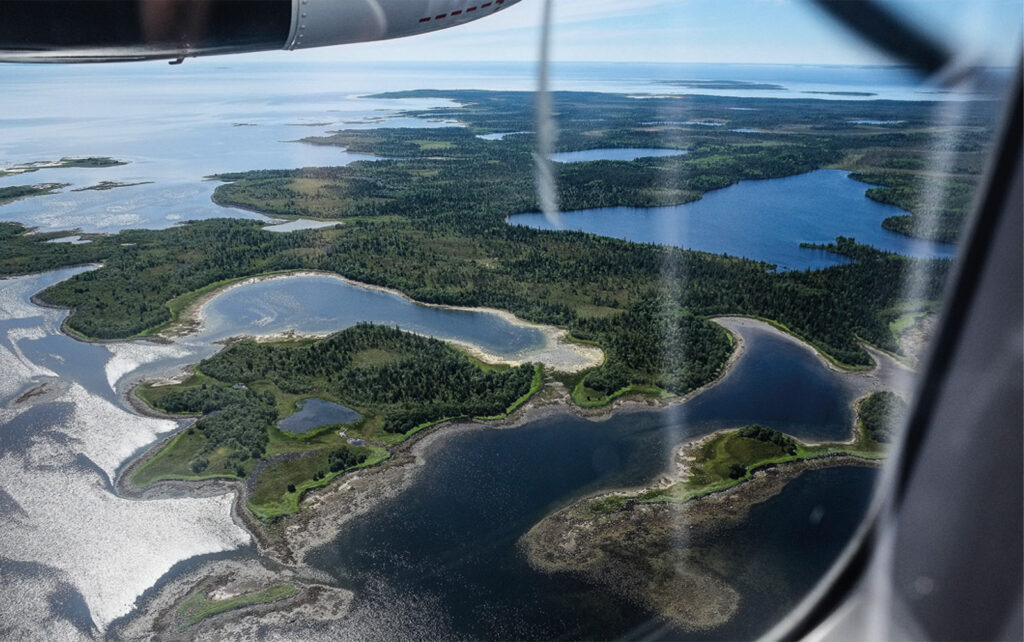 Lentokoneen ikkunasta kuvattu, näkyy vettä ja maata.