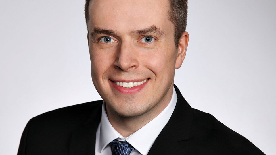 Mies katsoo kameraan ja hymyilee.