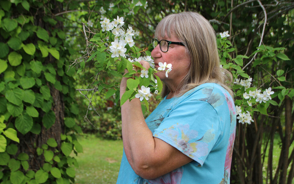 Nainen haistelee köynnöksen kukkia silmät kiinni.