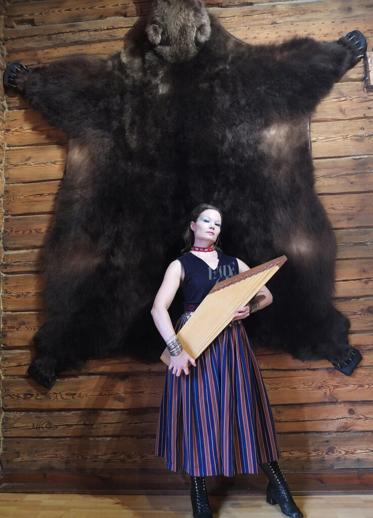 Nainen seisoo hirsiseinän edessä kannel sylissä.