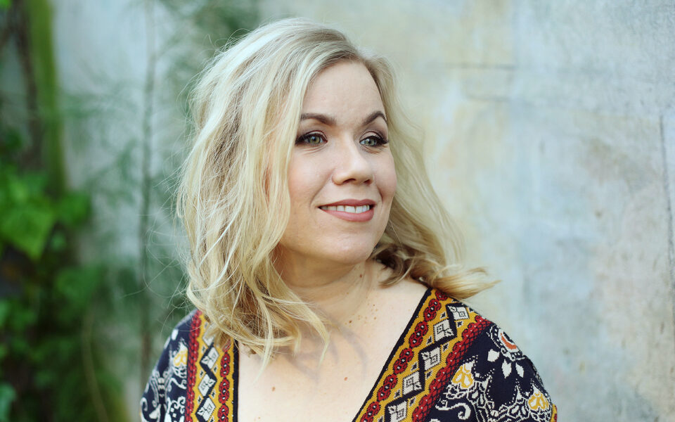 Nainen hymyilee ja katsoo olan yli kaukaisuuteen.