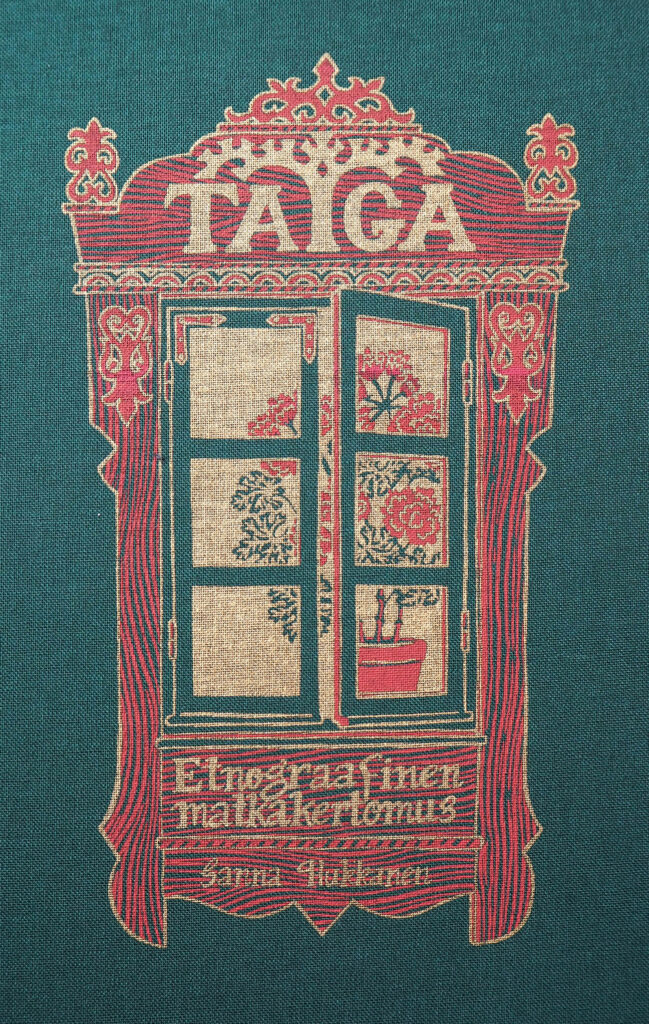 Kangaspintainen kirjankansi, jonka tummanvihreälle taustalle on piirretty pieniruutuinen ikkuna. Ikkunanpuitteet ovat punaiset, perinteisin puuleikkauksin koristellut. Kullanvärisellä tekstillä on kirjoitettu kirjan tiedot: Taiga. Etnograafinen matkakartomus. Sanna Hukkanen. Raotetusta ikkunasta avautuu kullattu tausta, jota vasten piirtyy punainen pelargonia., 