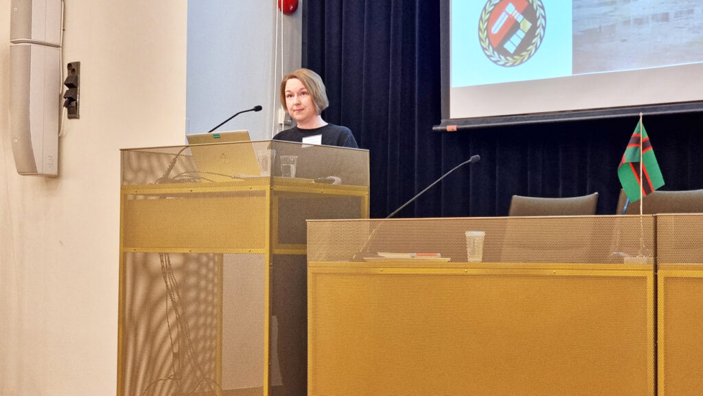 Nainen puhuu mikrofoniin puhujankorokkeella.