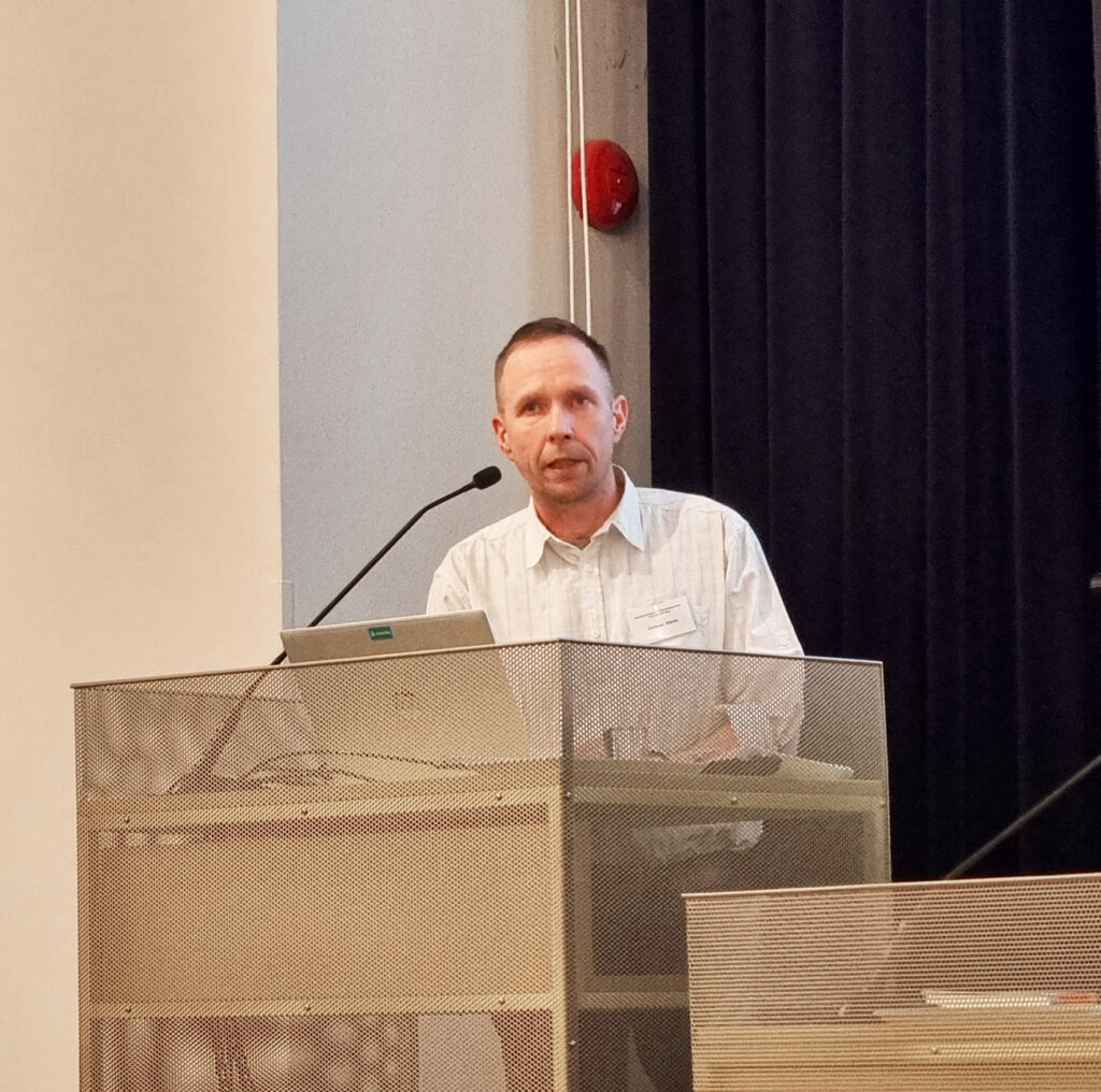 Mies puhuu mikrofoniin puhujankorokkeella.