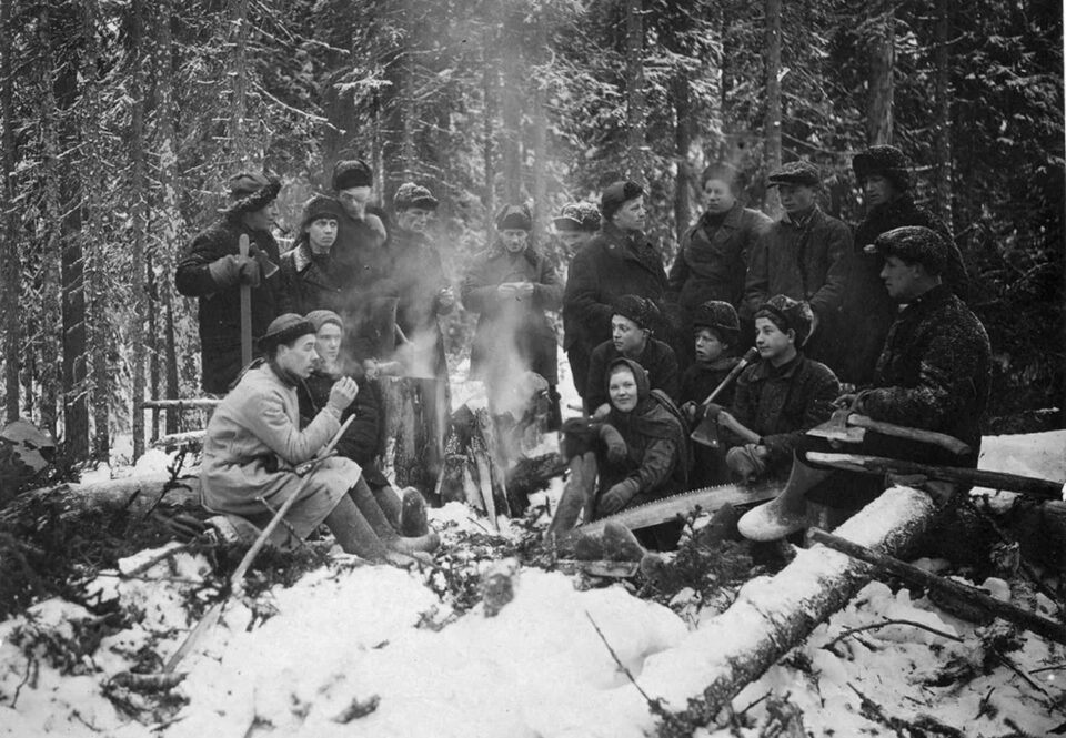Mustavalkoisessa valokuvassa ryhmä metsätyöläisiä taukotulilla.