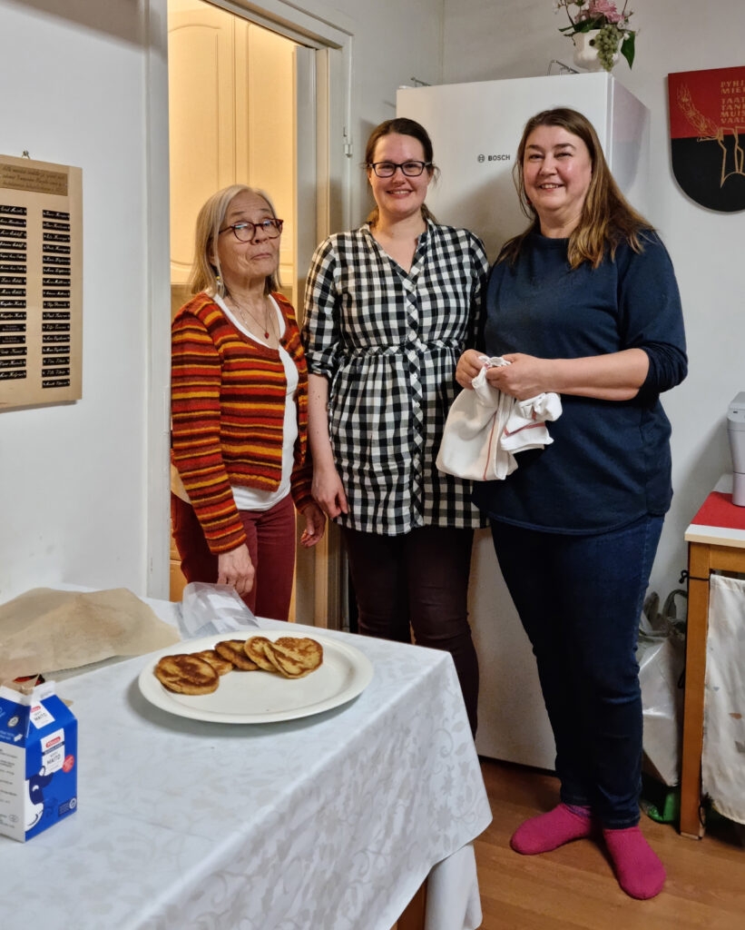 Kolme iloisesti hymyilevää naista katsoo kohti kameraa.