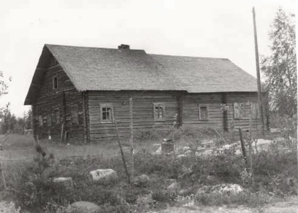 Vanha harmaa hirsirakennus sivustapäin kuvattuna.