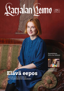 Aikakauslehden kansikuva, jossa nuorehko, siniseen pitkähihaiseen mekkoon pukeutunut nainen istuu jugend-tyylisellä sohvalla ja katsoo hymyillen suoraan kameraan. Seinä taustalla on viininpunainen ja siihen on maalattu antiikin aikaan viittaava, toogaan pukeutunut hahmo.