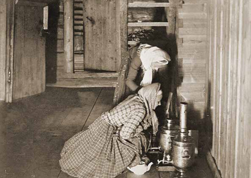 Vanhassa mustavalkokuvassa kaksi huivipäistä, perinteisiin vienankarjalaisiin arkiasuihin pukeutunutta naista tarkkailee kahta lattialla olevaa kiiltävää samovaaria. Toinen naisista on kumartunut samovaareja kohti, toinen on kyykyssä lattialla niiden edessä.