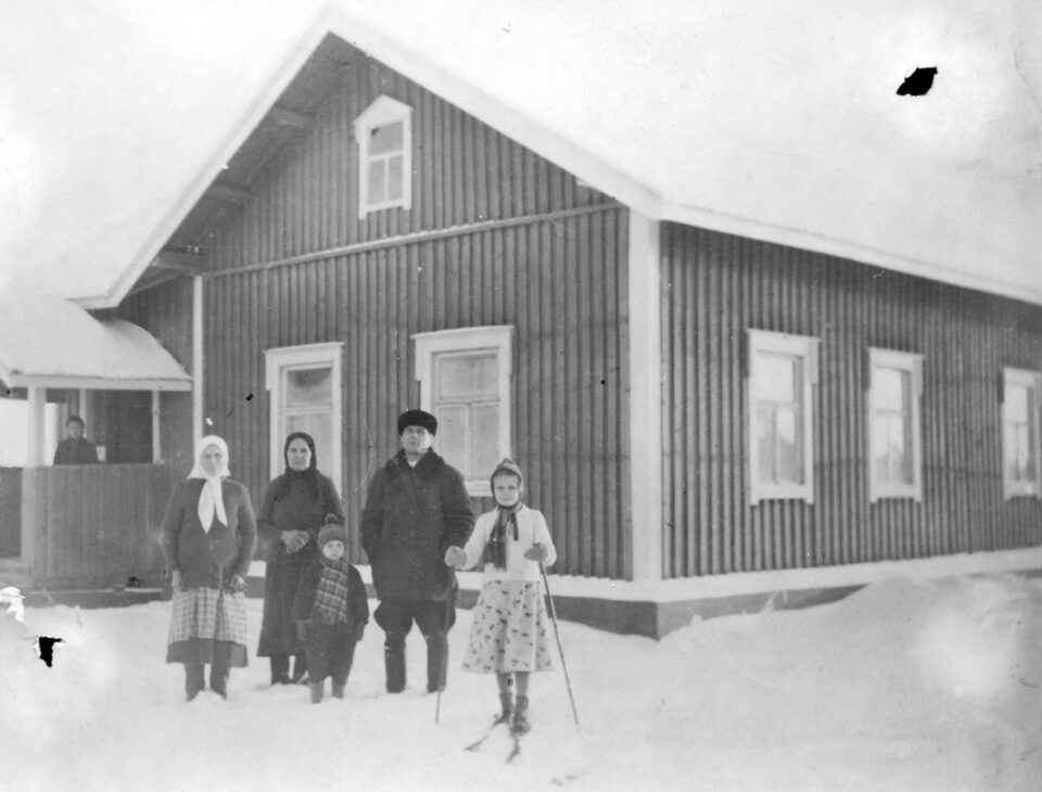Vanhassa mustavalkoisessa valokuvassa rintamamiestalon edustalla seisoo viisihenkinen perhe talvivaatteissaan. Oikeassa reunassa tytöllä on jaloissaan sukset ja käsissään sauvat. Myös talon kuistilla taempana häämöttää yksi henkilö.