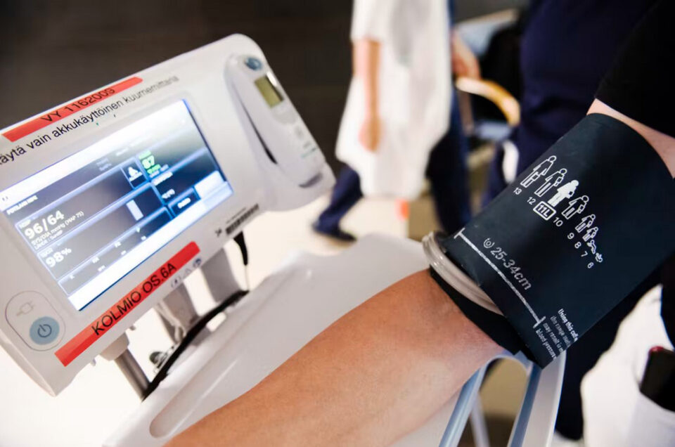 Lähikuvassa verenpaineen mittausta käsivarressa, lukemat näkyvät isolla digitaalisella näytöllä.