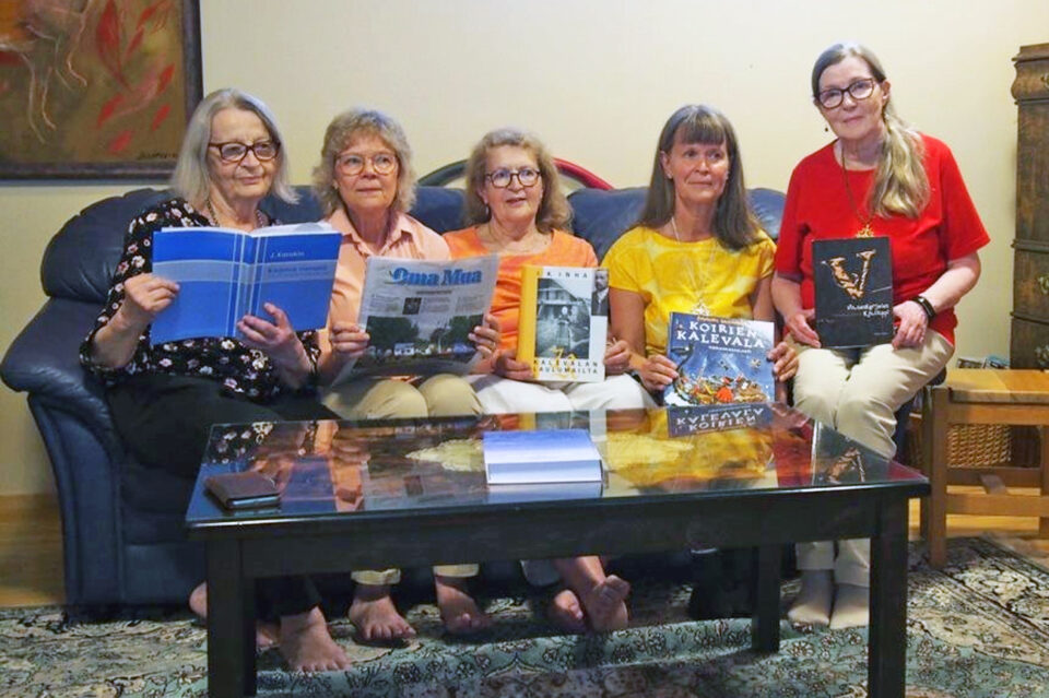 Viisi iloisen näköistä naista istuu rivissä sohvalla, kaikilla on kädessään tai sylissään jokin karjalankielinen julkaisu.