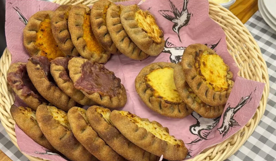 Korillinen perinteisiä karjalanpiirakoita sekä rönttösiä tarjoiltuna vaaleanpunaisen lintukuvioisen servietin päällä.