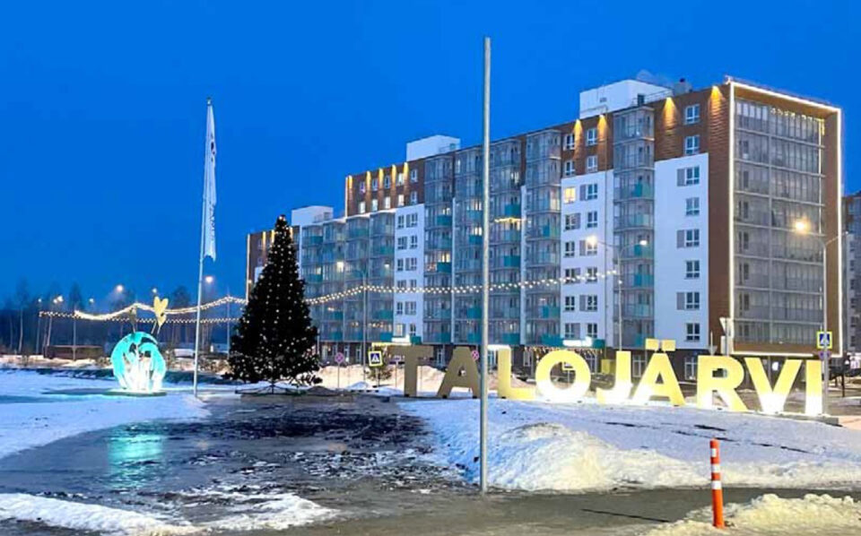 Sinisävyisessä talvikuvassa moderni laatikkomainen rakennus, jonka etualalla pari lipputankoa ja iso nimikyltti, jossa lukee "Talojärvi".