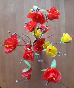 Kimppu värikkäästi punaisilla ja keltaisilla silkkipaperikukkasilla koristeltuja pajunoksia, joissa on mukana pajunkissoja.