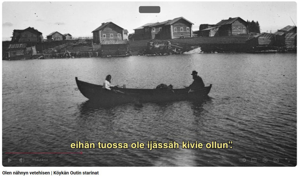 Vanha mustavalkoinen kuva, järvellä on pitkä soutuvene, jossa istuu kaksi ihmistä, soutaja ja peränpitäjä. Vesistön taustalla, kuvan taka-alalla kokoaa kylä taloineen.