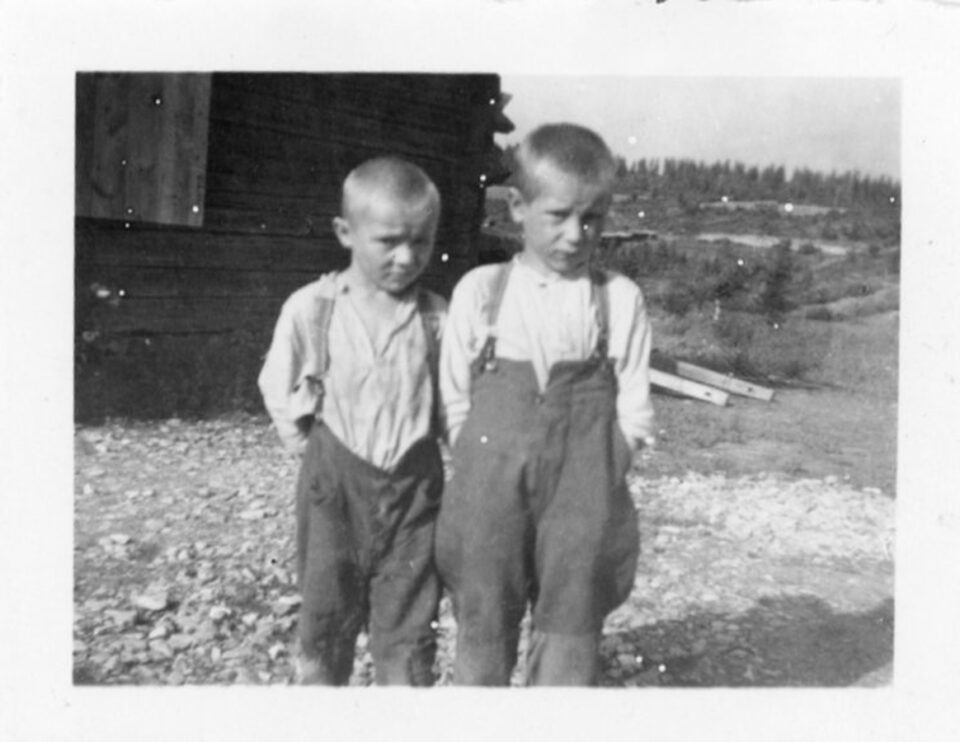 Vanhassa mustavalkoisessa valokuvassa kaksi pikkupoikaa seisoo vierekkäin totisina kesäisellä pihamaalla. Molemmilla on pussihousut, pitkähihainen vaalea paita ja henkselit. Katsovat kameraan alta kulmiensa.