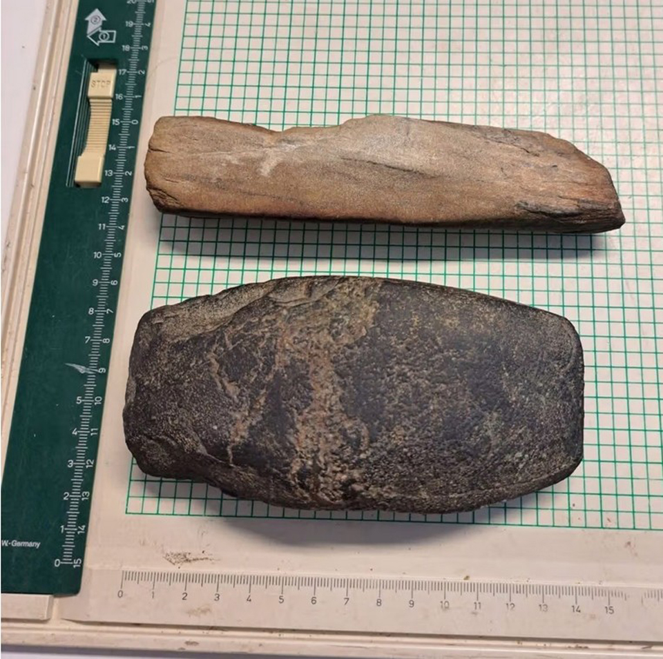 Millimetrimitoilla reunustetun ruutupaperin päällä lepää kaksi kivikautiselta näyttävää kiviesinettä allekkain. Ylempi on kapeampi, vaaleansävyinen, alempi on tumma, ehkä kivikirvestä muistuttava, hyvin tummanruskea.