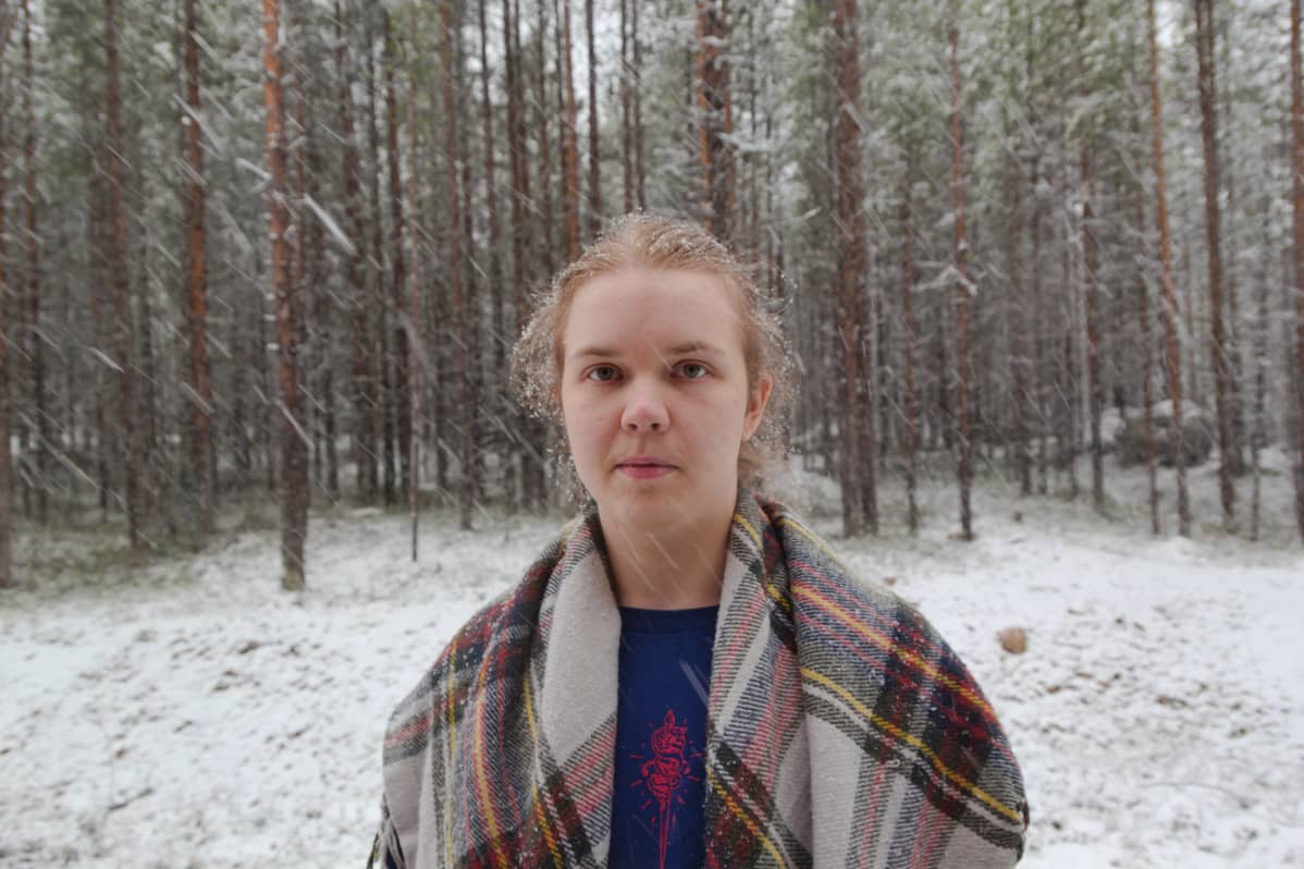 Nuori henkilö lumisateessa, taustalla metsää.