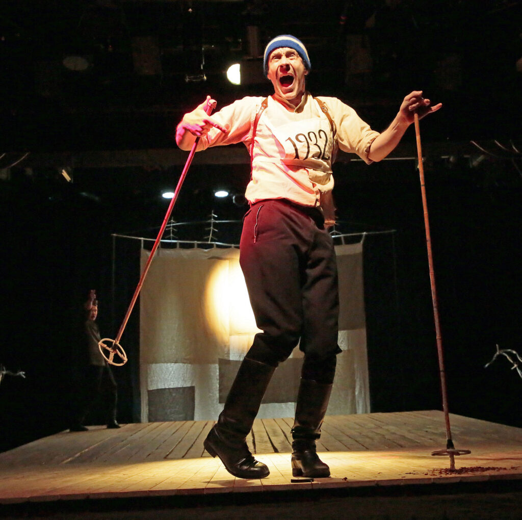 Mies esittää hiihtämistä teatterin lavalla.