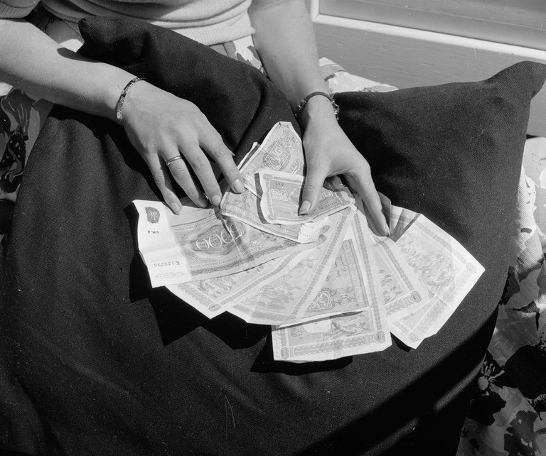 Mustavalkoinen kuva naisen käsistä tyynylle ja käsissä on seteleitä