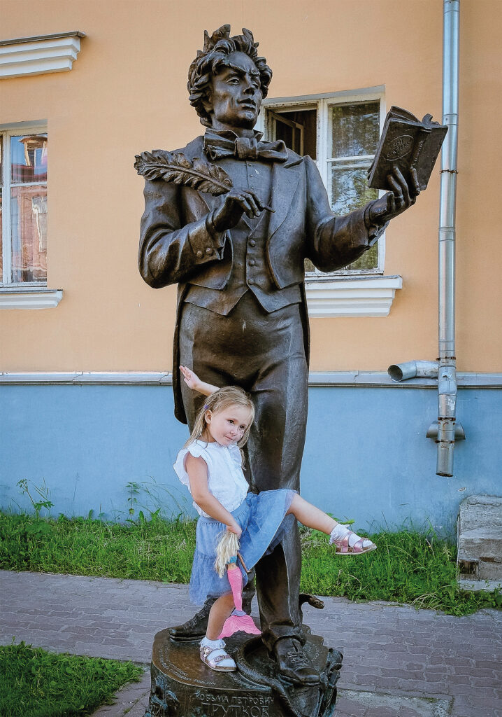 Pikkutyttö tasapainoilee ison patsaan jalustalla.