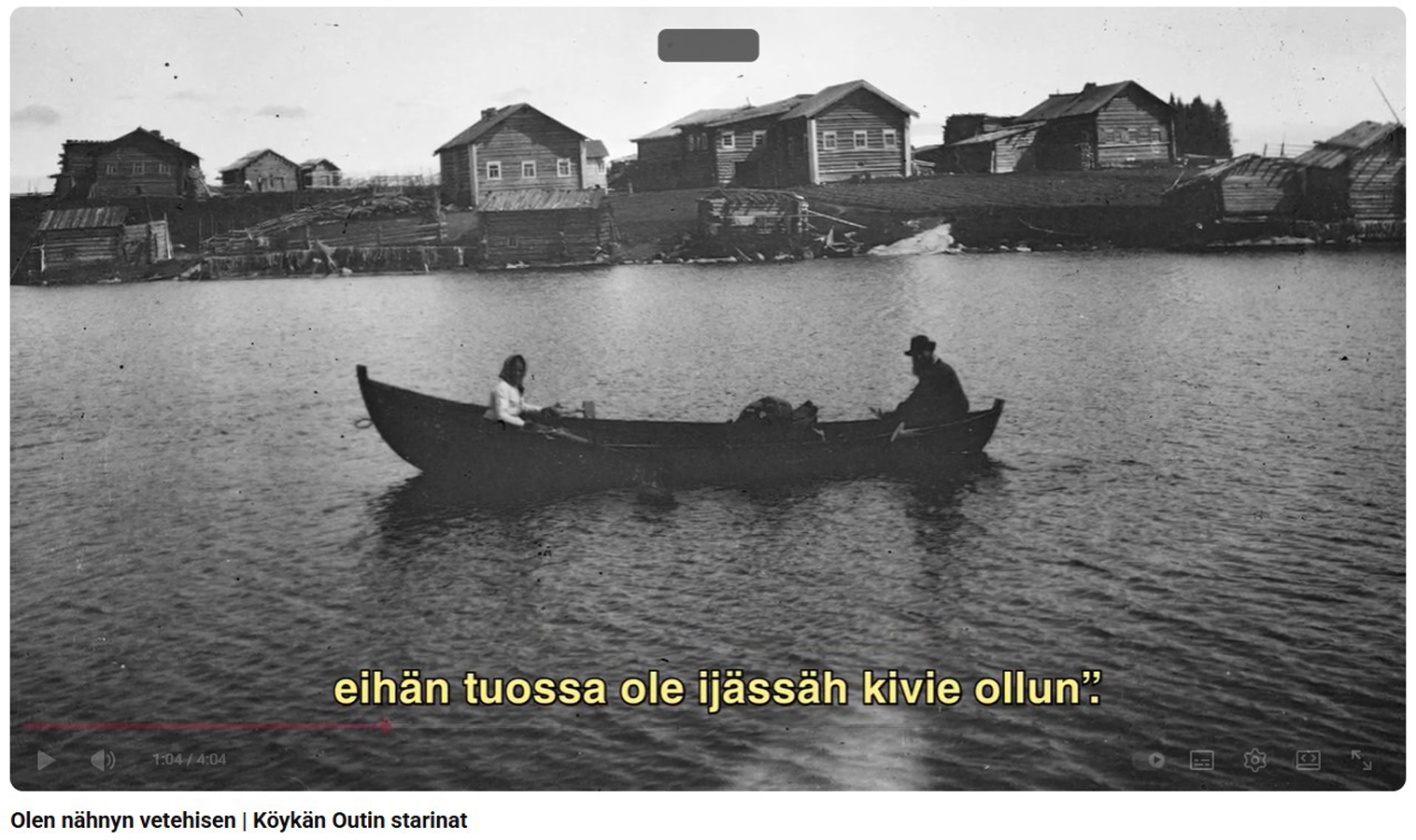 Vanha mustavalkoinen kuva, järvellä on pitkä soutuvene, jossa istuu kaksi ihmistä, soutaja ja peränpitäjä. Vesistön taustalla, kuvan taka-alalla kokoaa kylä taloineen.